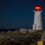 Peggy's Cove at Night, a white lighthouse with red top and light shining in the dark